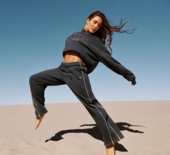 Model poses in a dark grey GARAGE branded sweater and matching sweats.