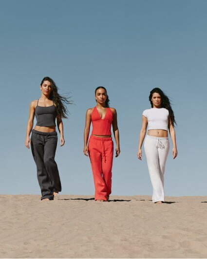 Three models pose in matching outfits, one in grey, one in dark grey, and the last in orange.