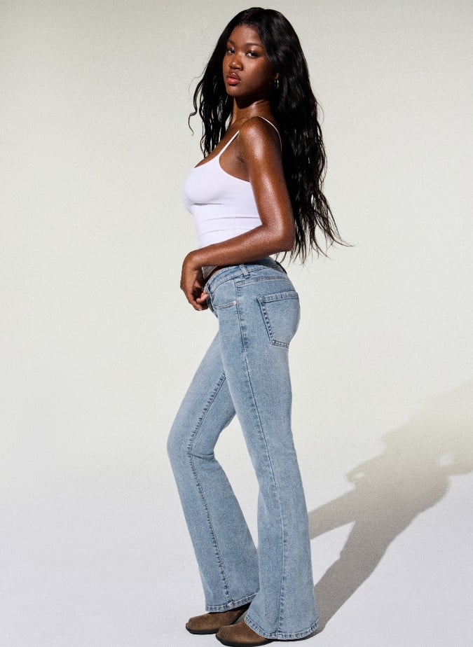 La mannequin porte une camisole blanche et un jean bleu pâle évasé.