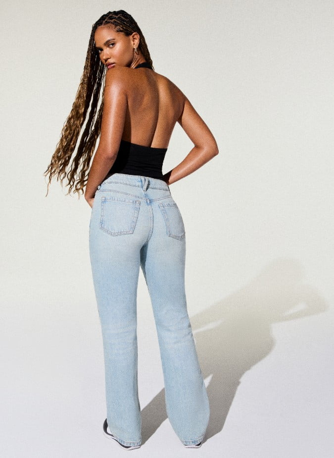 La mannequin porte un justaucorps noir et un jean usé bleu pâle.