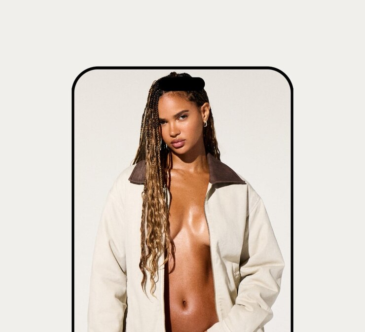 Model poses in a white worker jacket with no shirt underneath and light wash denim.