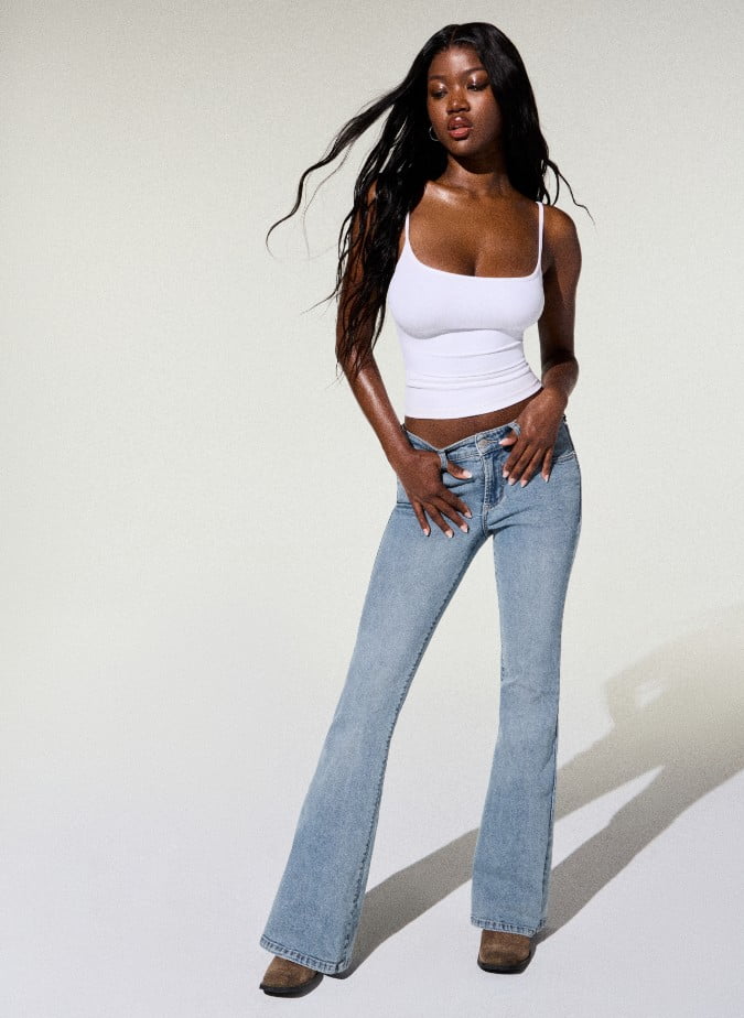Model poses in a white tank top and light wash flared jeans.