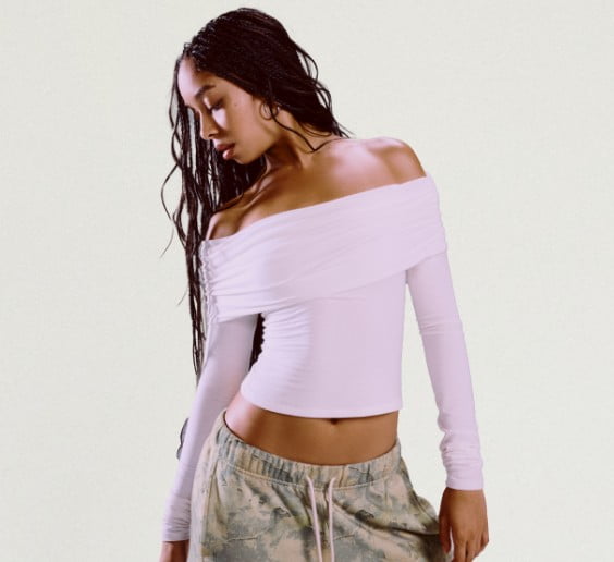 Model poses in a white, long sleeve, off the shoulder top and camo sweats.