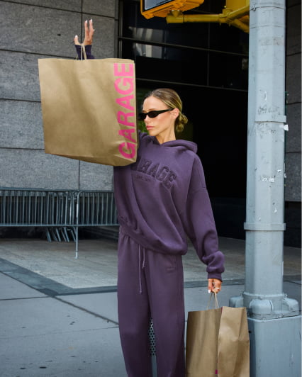 Hallie Batchelder poses with shopping bags wearing a purple hoodie and matching sweats.