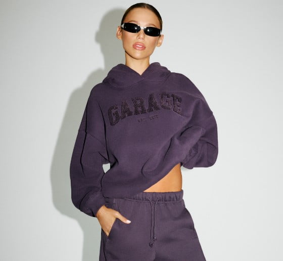Hallie Batchelder poses in sunglasses, a purple GARAGE sweater, and matching sweats.