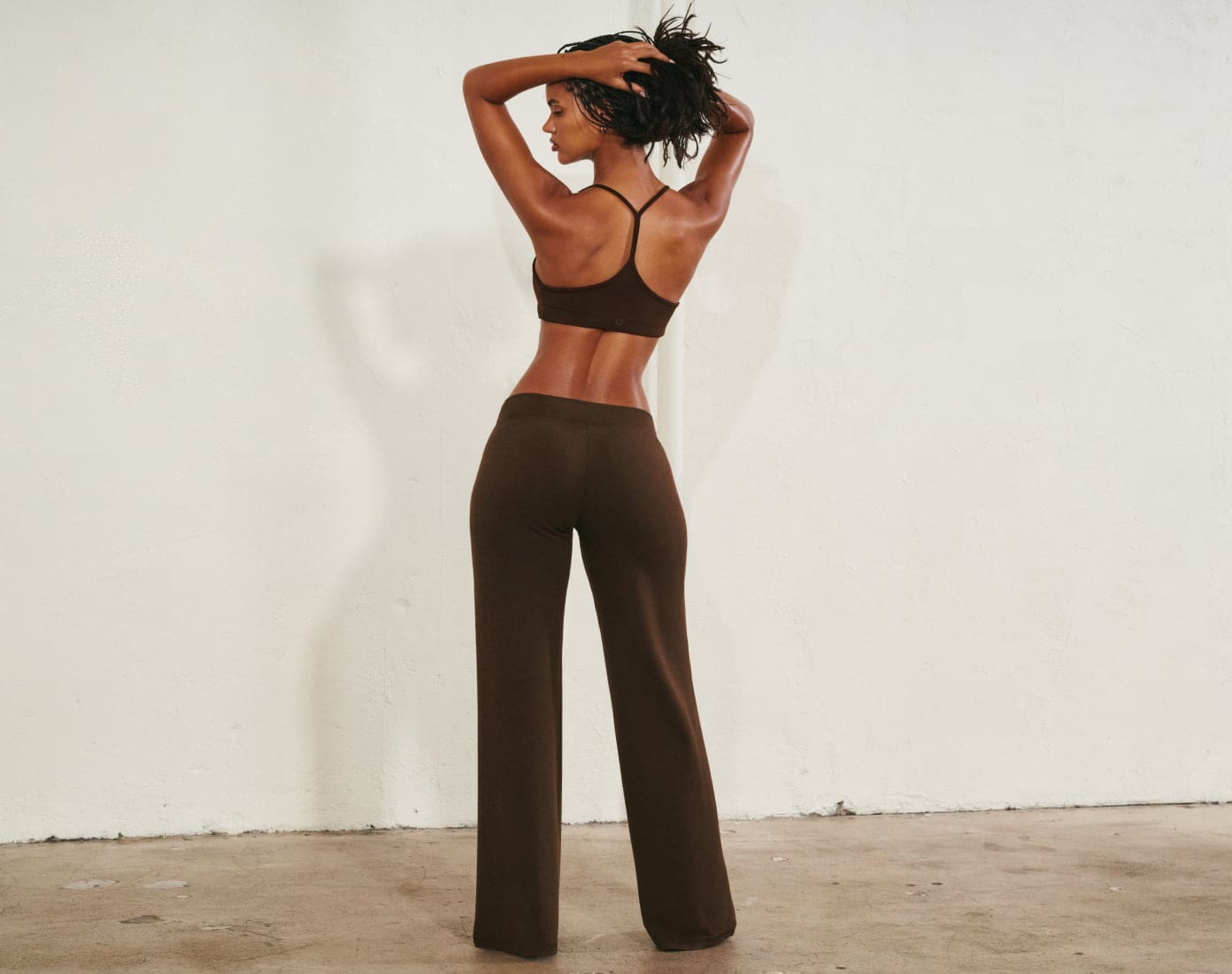 Model poses in a brown sports bra and matching sweats.